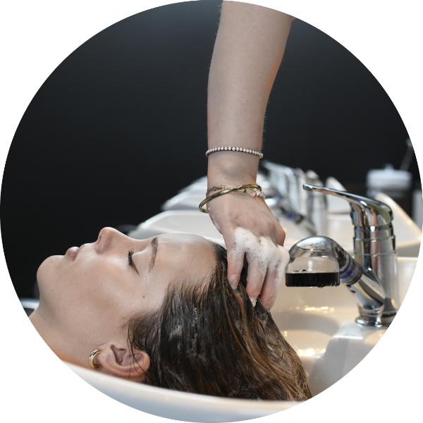 A woman getting her hair washed in a sink equipped with eco head shampoo heads reducing water waste