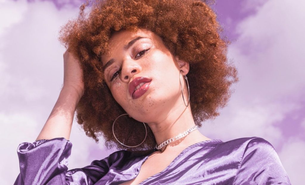 A woman with afro hair posing against a cloudy sky.